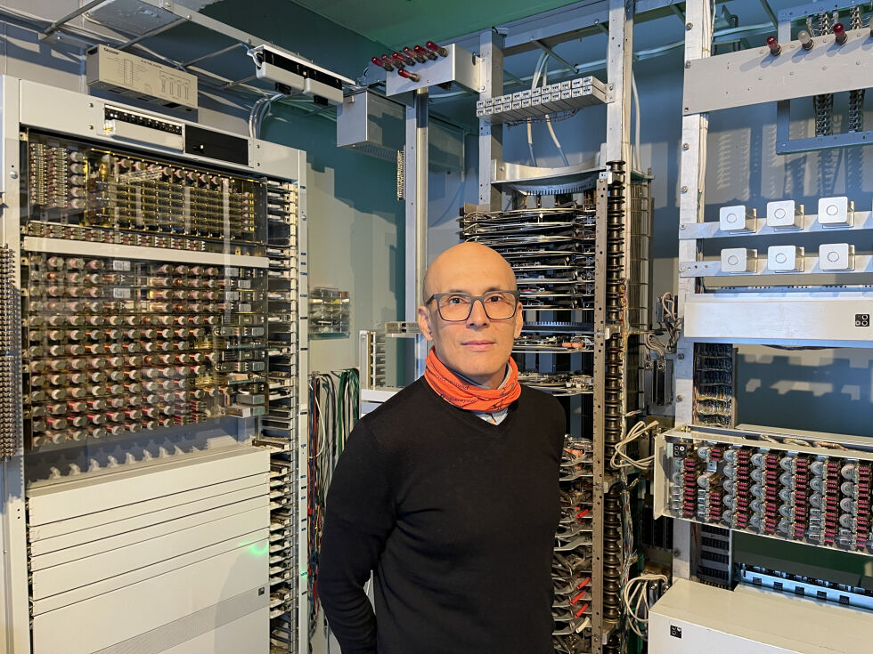 Bak ham ser vi en imponerende samling av gammelt telekommunikasjonsutstyr, en del av hans dedikerte arbeid med å bevare og dokumentere telehistorien.
 Foto: Renate Rosenvinge