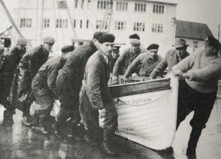Kaiarbeidere og frivillige på havna i Rørvik frakter travaljebåten fra skipet til en lagringsplass.
 Foto: Fra boka "Mayday fra St. Svithun"